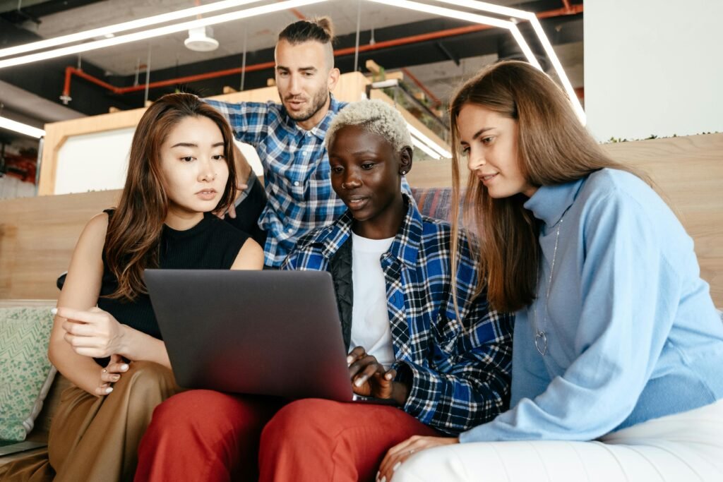 Group of young female and male colleagues checking netbook together in modern workspace in daytime